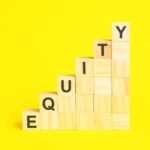 Wooden blocks stacked to form a staircase, with the word "EQUITY" spelled vertically using black letters on the blocks, against a bright yellow background.